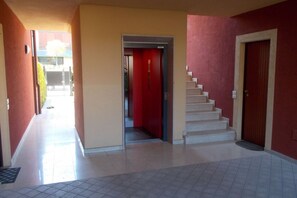 A hallway with a red door, a staircase, and a view of a building outside.
