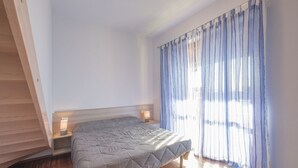 A bedroom with a bed, wooden flooring, a nightstand with a lamp, and a window with curtains. - Orchid Three-room apartment with large terrace, pool and WiFi (Sirmione)