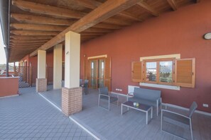 An outdoor patio area with wooden beams, a brick column, and a seating arrangement with two chairs and a table.