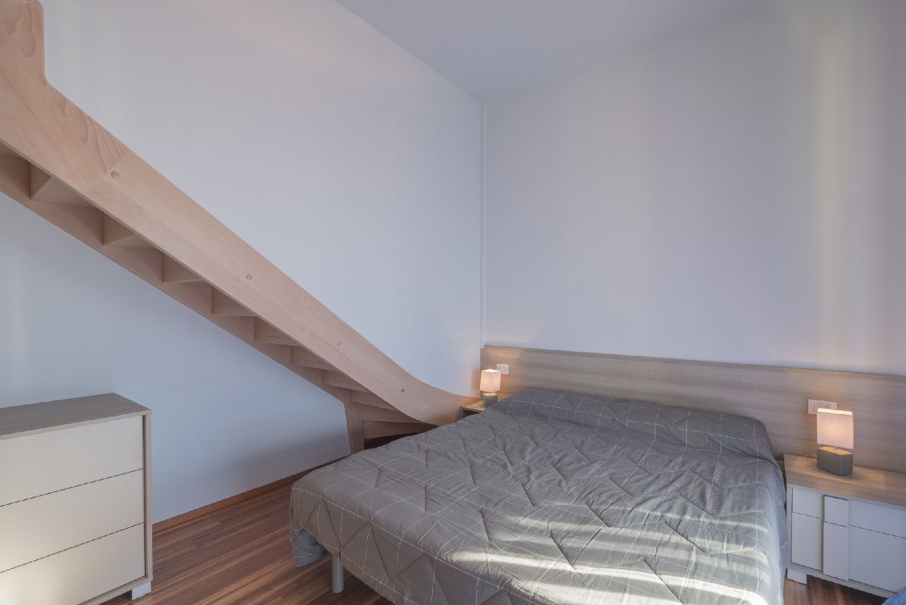 Une chambre à coucher comprenant un lit, une table de chevet, une commode et un escalier en bois.