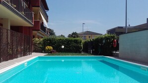 A swimming pool with a clear blue water, surrounded by a fence and a hedge. - Orchid Three-room apartment with large terrace, pool and WiFi (Sirmione)