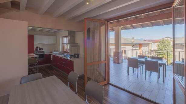 A modern kitchen with red cabinets and a dining area with a table and chairs. - Orchid Three-room apartment with large terrace, pool and WiFi (Sirmione)