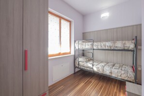 A room with a bunk bed, wooden wardrobe, and a window with curtains.