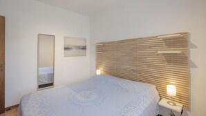 A bedroom with a bed, a bedside lamp, a wooden slat headboard, a mirror, and a framed picture on the wall.