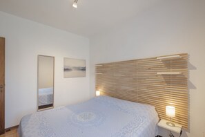 Un dormitorio con cama, lámpara de noche, cabecera de listones de madera, espejo y un cuadro en la pared.