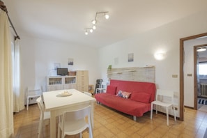 A small, well-lit room with a white table and chairs, a red sofa, and a television on a cabinet.