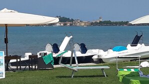 A lakeside setting with lounge chairs and umbrellas, boats, and a distant view of a town.