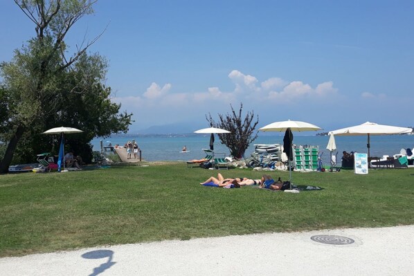 Una playa con sombrillas, sillas de descanso y una zona verde.