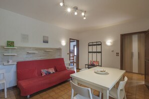 A living room with a red sofa, a white dining table, and a kitchen area with cabinets and a refrigerator.