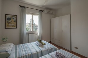 A hotel room with two beds, a wardrobe, a radiator, and a window with curtains.