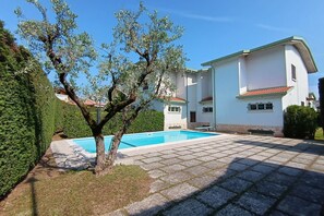 A residential property with a swimming pool, a white building with a red roof, and a well-maintained garden.