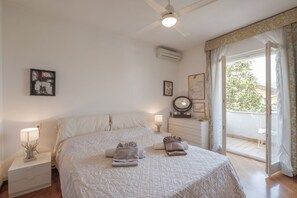 Un dormitorio con cama, mesitas de noche, ventilador de techo, aire acondicionado, ventana con cortinas y vistas al exterior.