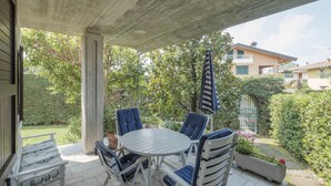 Un patio al aire libre con una mesa redonda y sillas azules, rodeado de follaje y vistas a casas vecinas.
