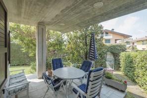 Un patio al aire libre con una mesa redonda y sillas azules, rodeado de follaje y vistas a casas vecinas.