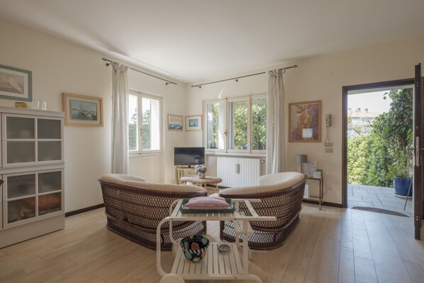Un salón acogedor con muebles de mimbre, un televisor y vistas al verde exterior.