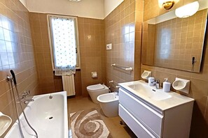 Un baño con bañera, inodoro, bidé, lavabo y espejo.