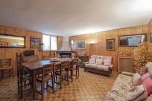 A wooden-paneled room with a dining table, chairs, a sofa, and a television.