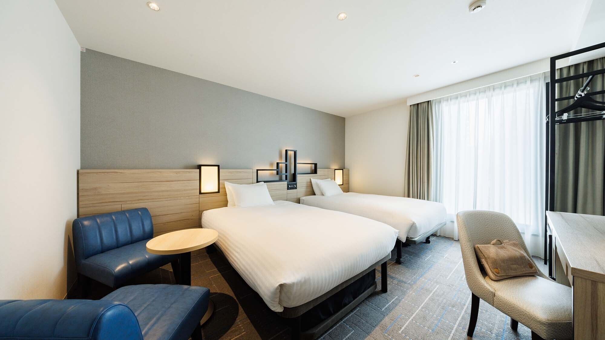 A hotel room with two beds, a blue sofa, a small round table, and a chair.