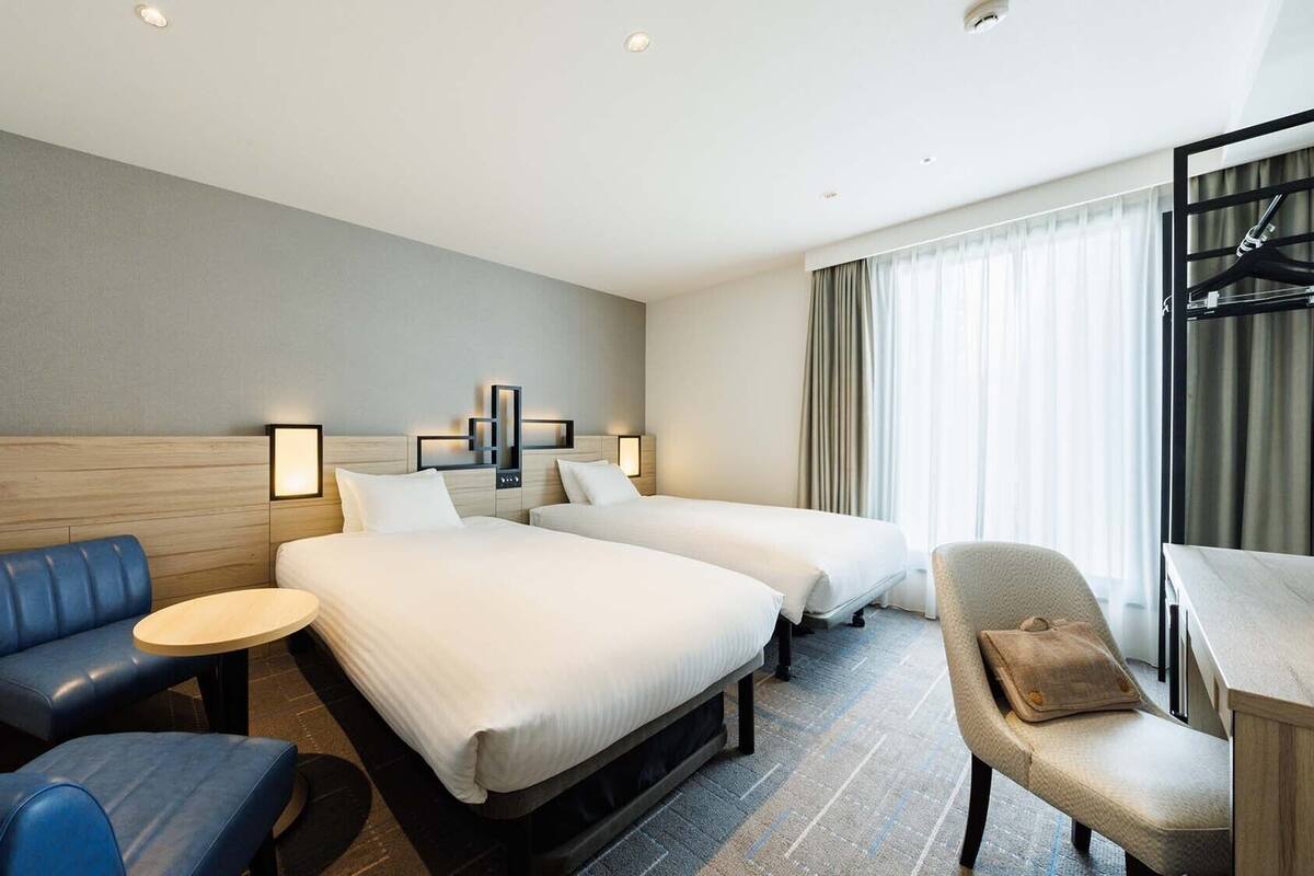 Ein Hotelzimmer mit zwei Betten, einem blauen Sofa, einem kleinen runden Tisch und einem Sessel.