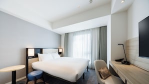 Quarto de hotel com cama, escrivaninha, cadeira, mesa redonda e televisão.