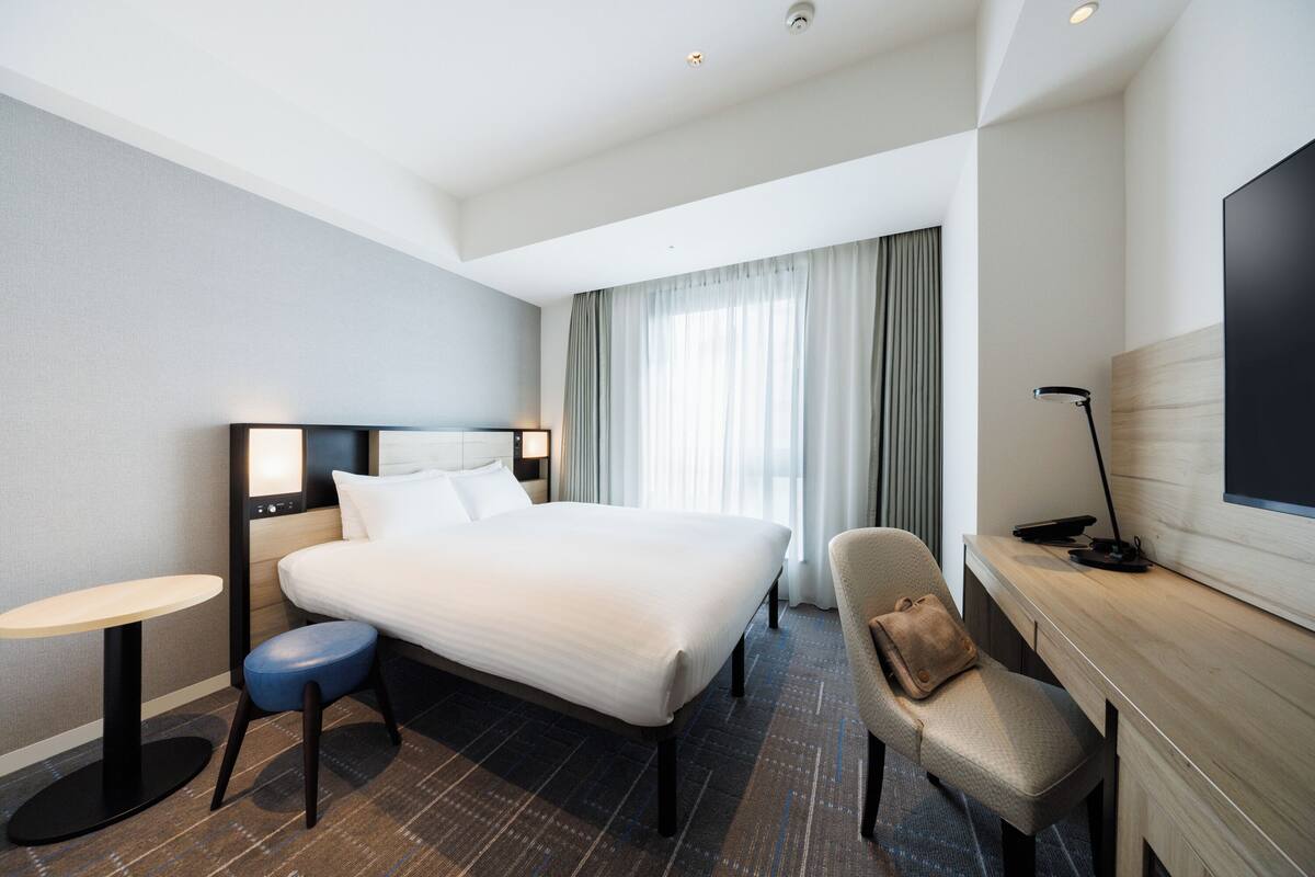 Ein Hotelzimmer mit Bett, Schreibtisch, Stuhl, rundem Tisch und Fernseher.