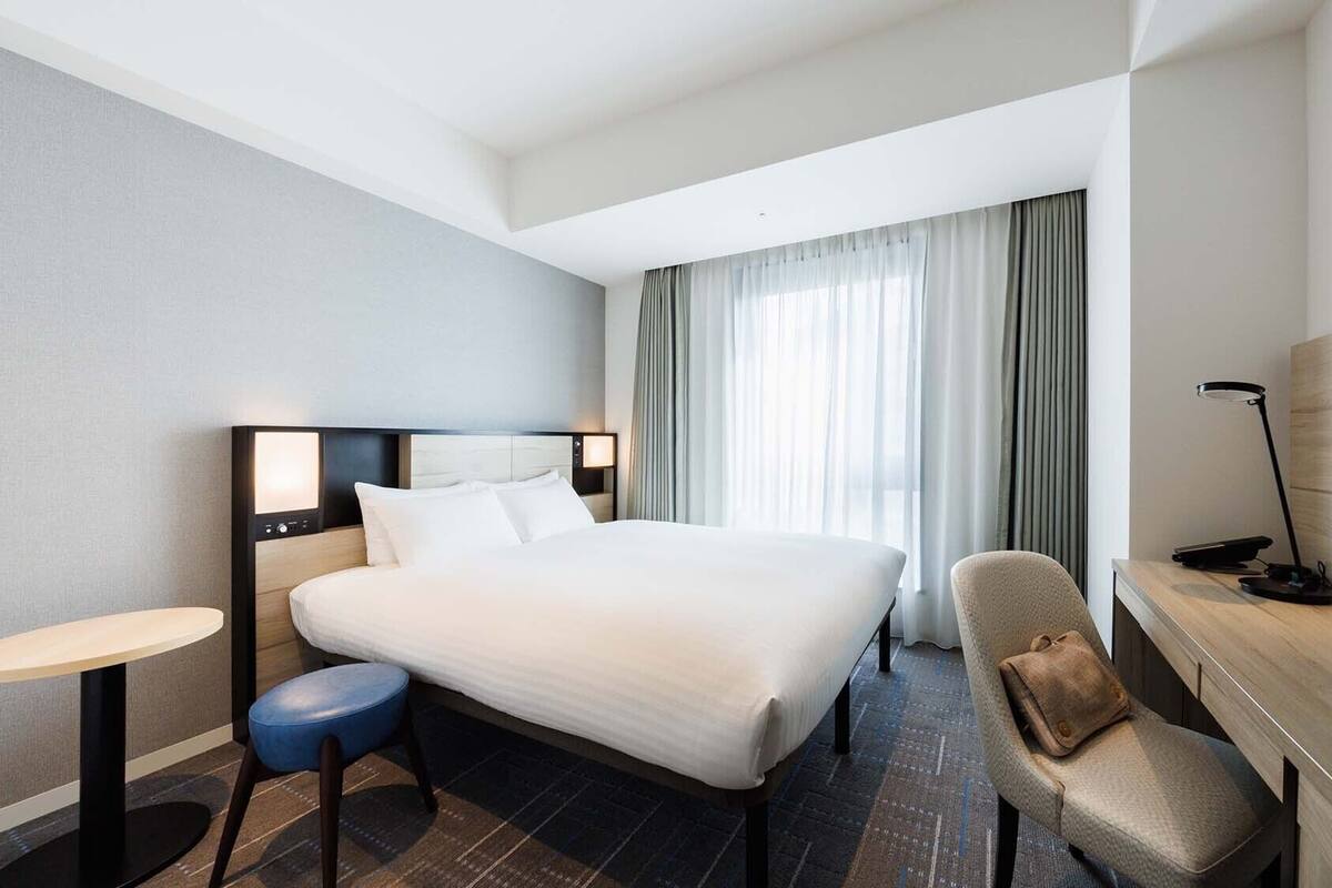 Ein Hotelzimmer mit einem großen Bett, einem Schreibtisch, einem Sessel, einer Lampe und einem Fernseher.