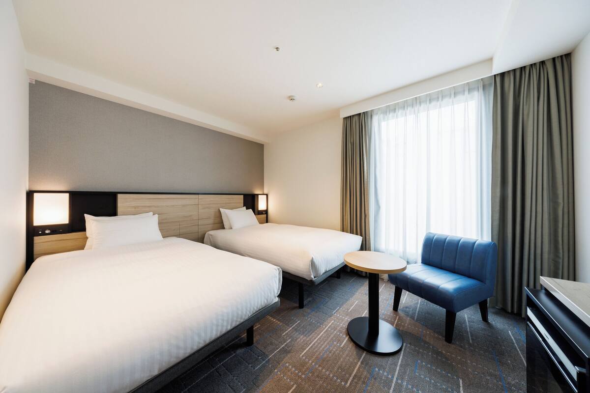 Ein Hotelzimmer mit zwei Betten, einem kleinen runden Tisch, einem blauen Sofa und einem Fernseher.