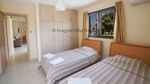 Une chambre avec deux lits, une armoire, une fenêtre avec des rideaux et un appareil de climatisation.