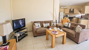 Un salon avec un téléviseur, un canapé, une table basse et une cuisine en arrière-plan.