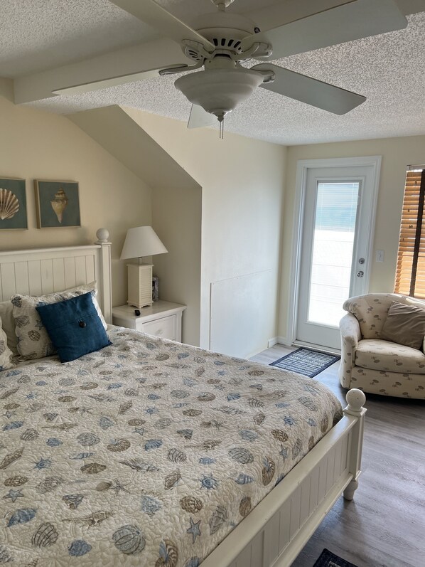 A bedroom with a bed, a nightstand, a chair, a ceiling fan, and a door with blinds. - On the beach,Pool,Pet Friendly,Tennis/Pickleball,Kayaks,Paddle boards,Bikes (Englewood)