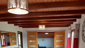 A cozy room with a wooden ceiling, a large sofa, a dining table with chairs, a wooden cabinet, and a mirror. - Family chalet with sauna for 10-12 people (Gérardmer)