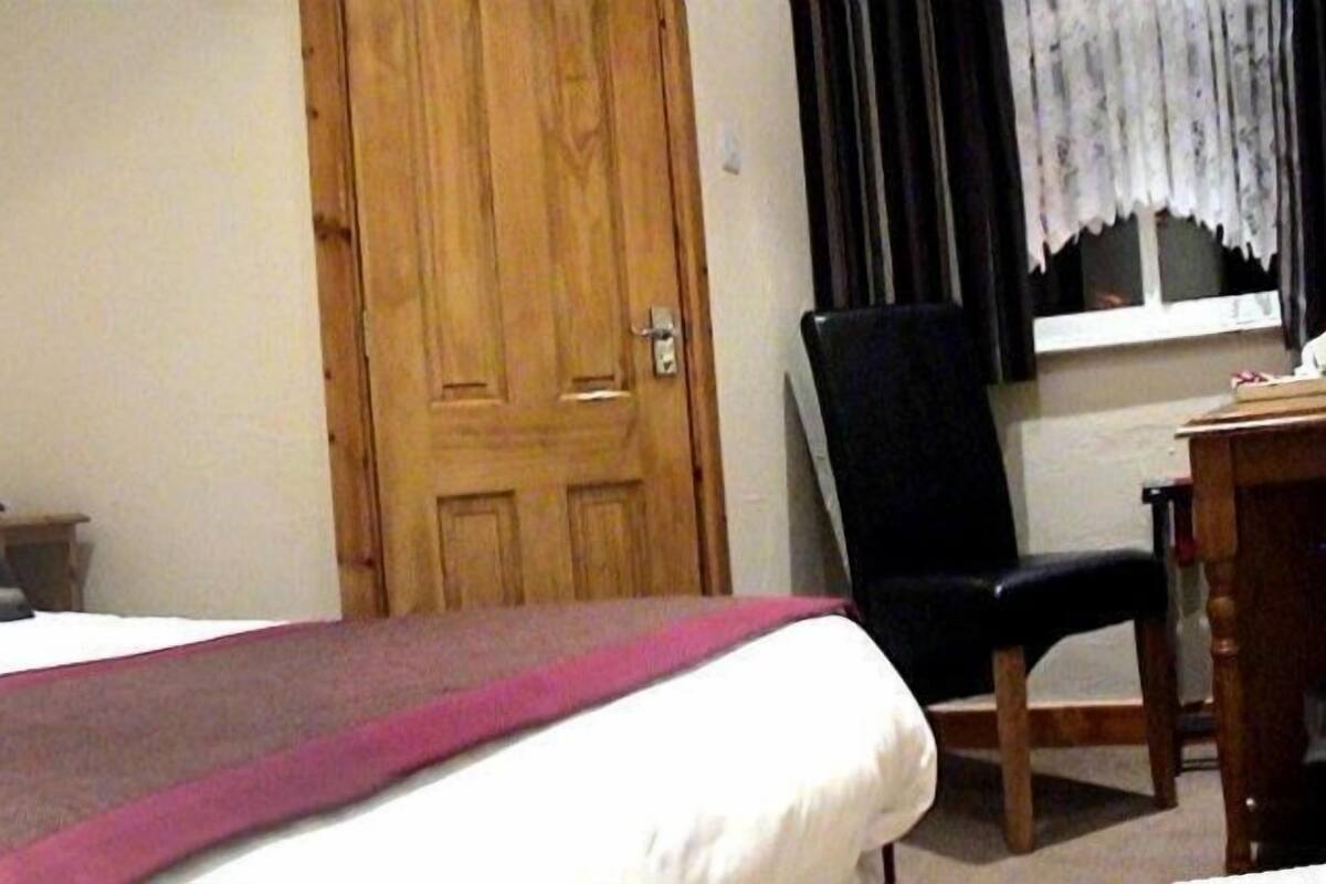 A bedroom with a bed, a wooden door, a desk, and a chair.