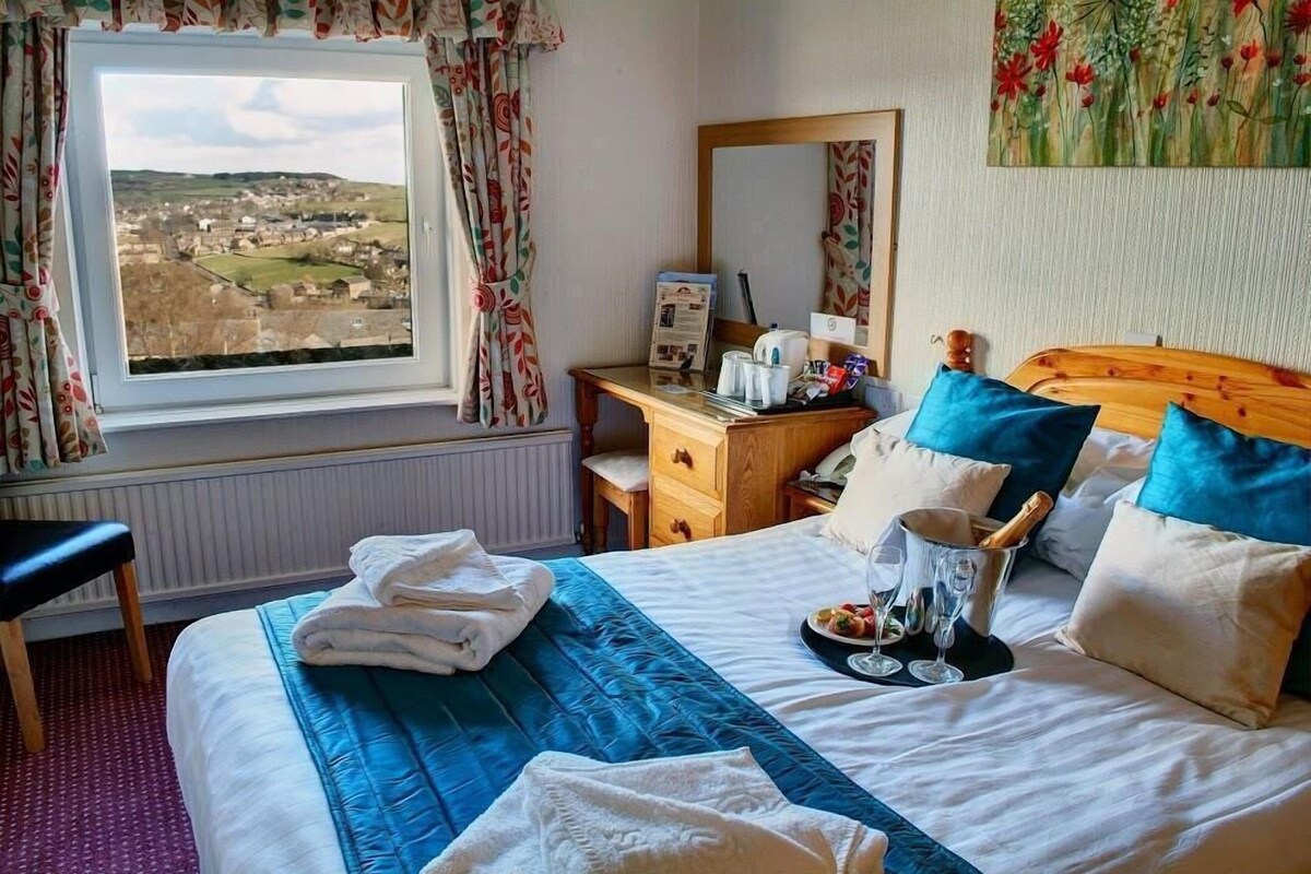 A hotel room with a bed, a desk, a chair, a window with a view, and a painting on the wall.
