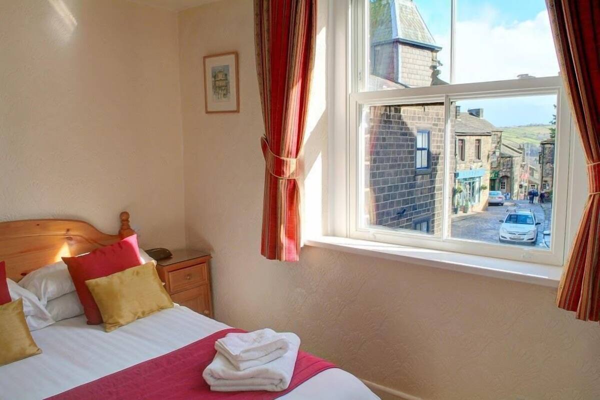 A bedroom with a bed, a nightstand, a window with curtains, and a view of a street.