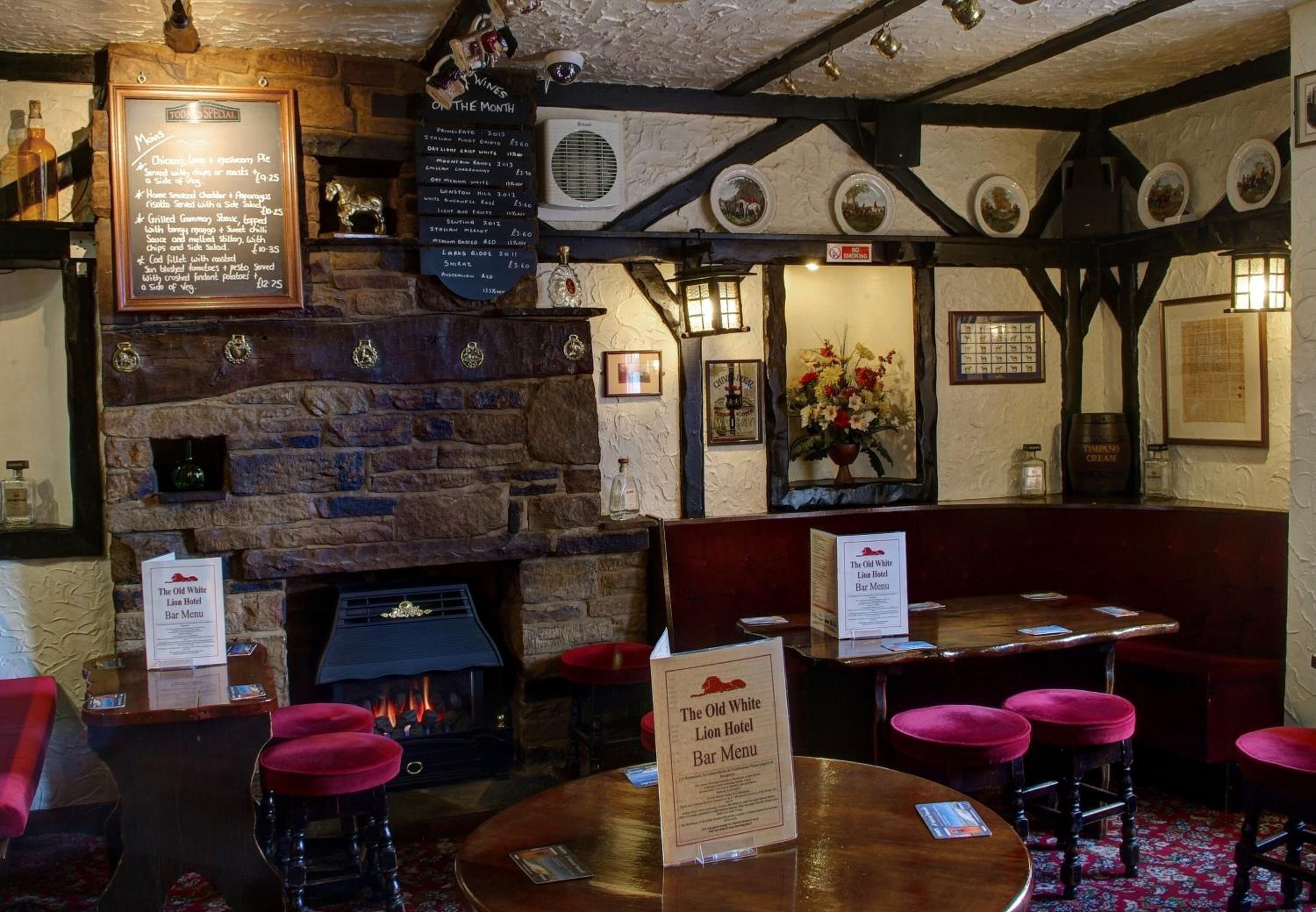 A traditional pub interior with stone walls, a fireplace, wooden tables, and red bar stools.