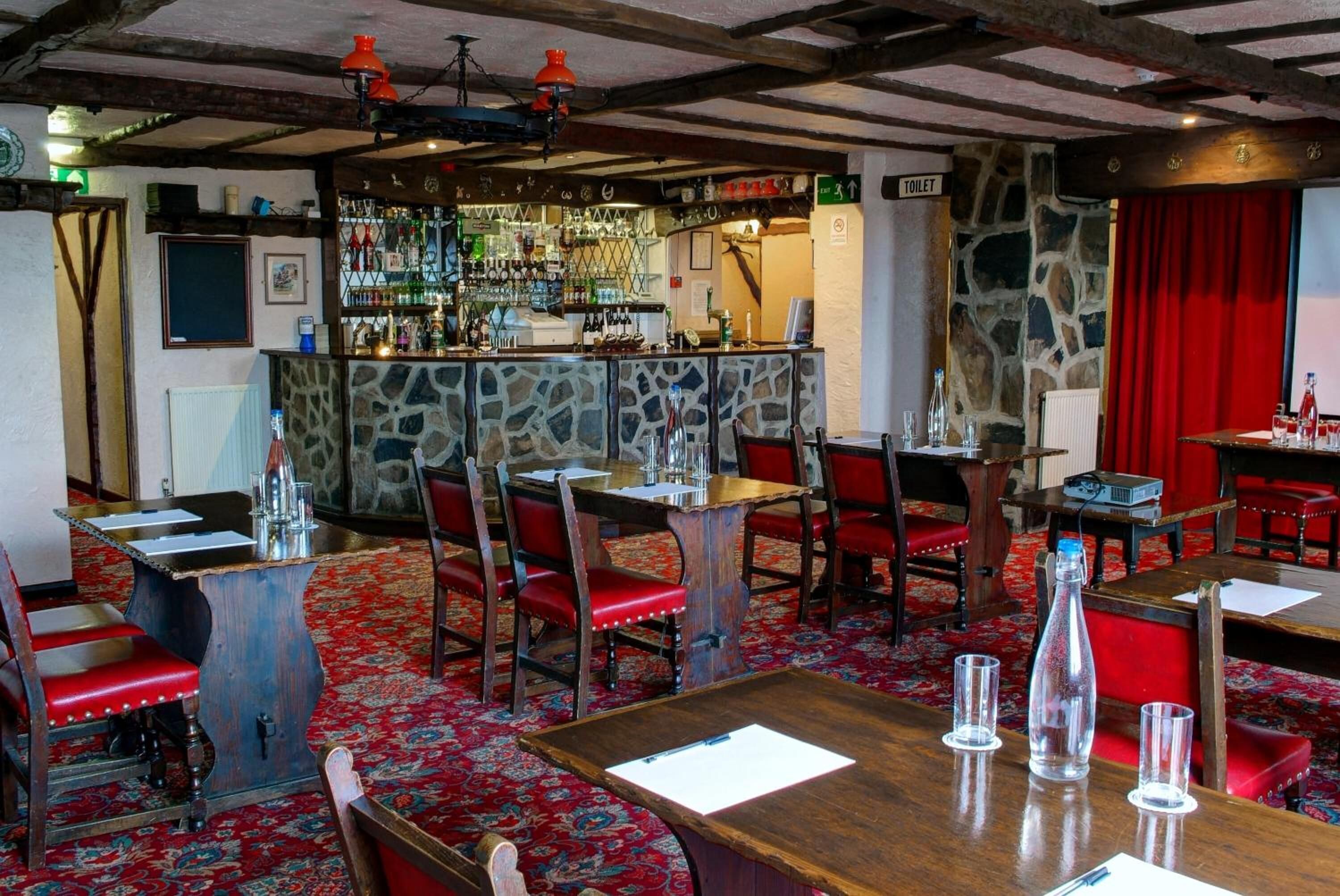 A restaurant with a stone wall bar, red upholstered chairs, and a red carpeted floor.