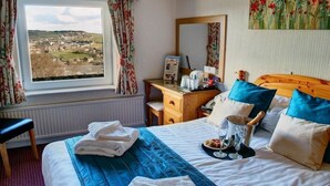 Ein Hotelzimmer mit einem großen Bett, einem Schreibtisch, einem Stuhl, einem Fenster mit Blick auf eine Stadt und einem Bild an der Wand.