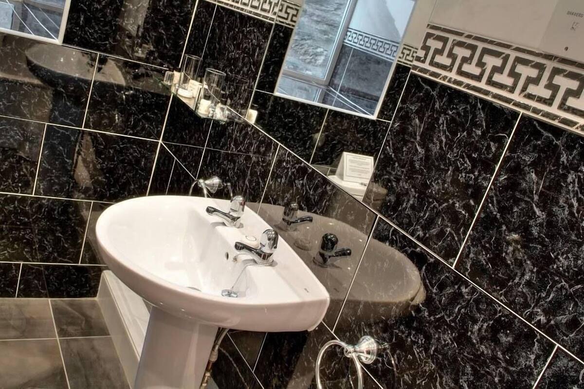 A bathroom with a white sink, black marble tiles, and a decorative border.
