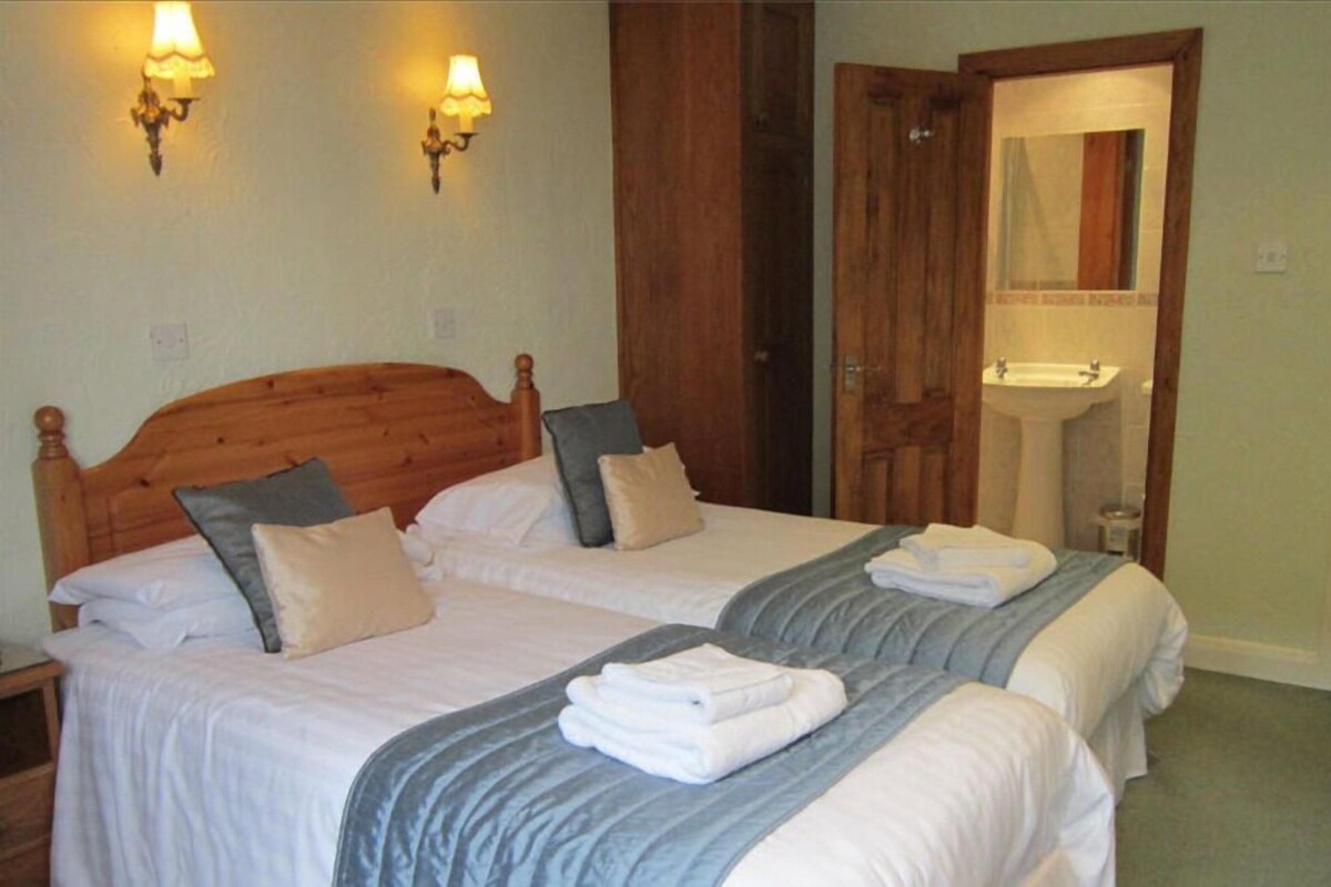 A double room with two beds, a wooden headboard, a bathroom with a sink and mirror, and wall-mounted lights.