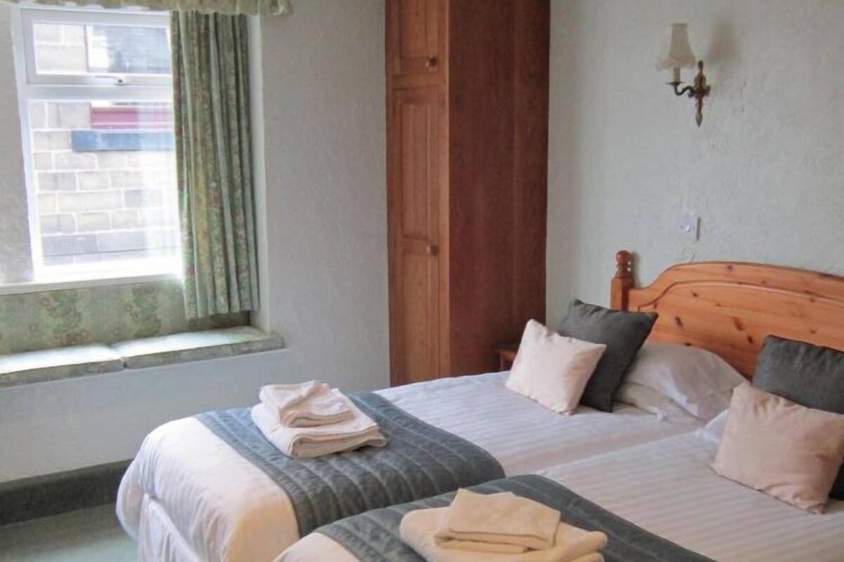 A double bed with a wooden headboard, two pillows, and folded towels on each side.