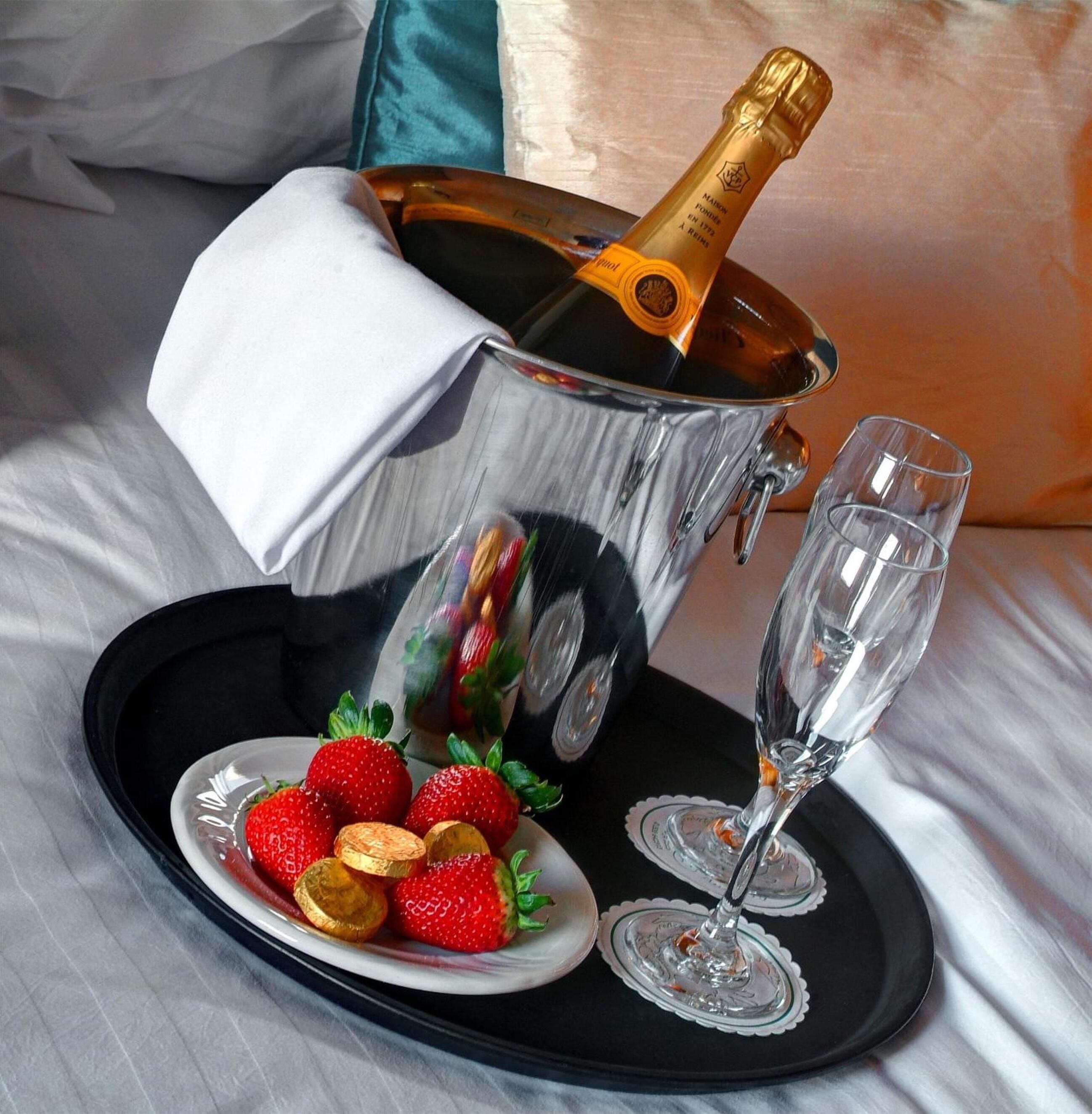 A champagne bottle in a silver bucket, two glasses, and a plate with strawberries and chocolate coins on a tray.
