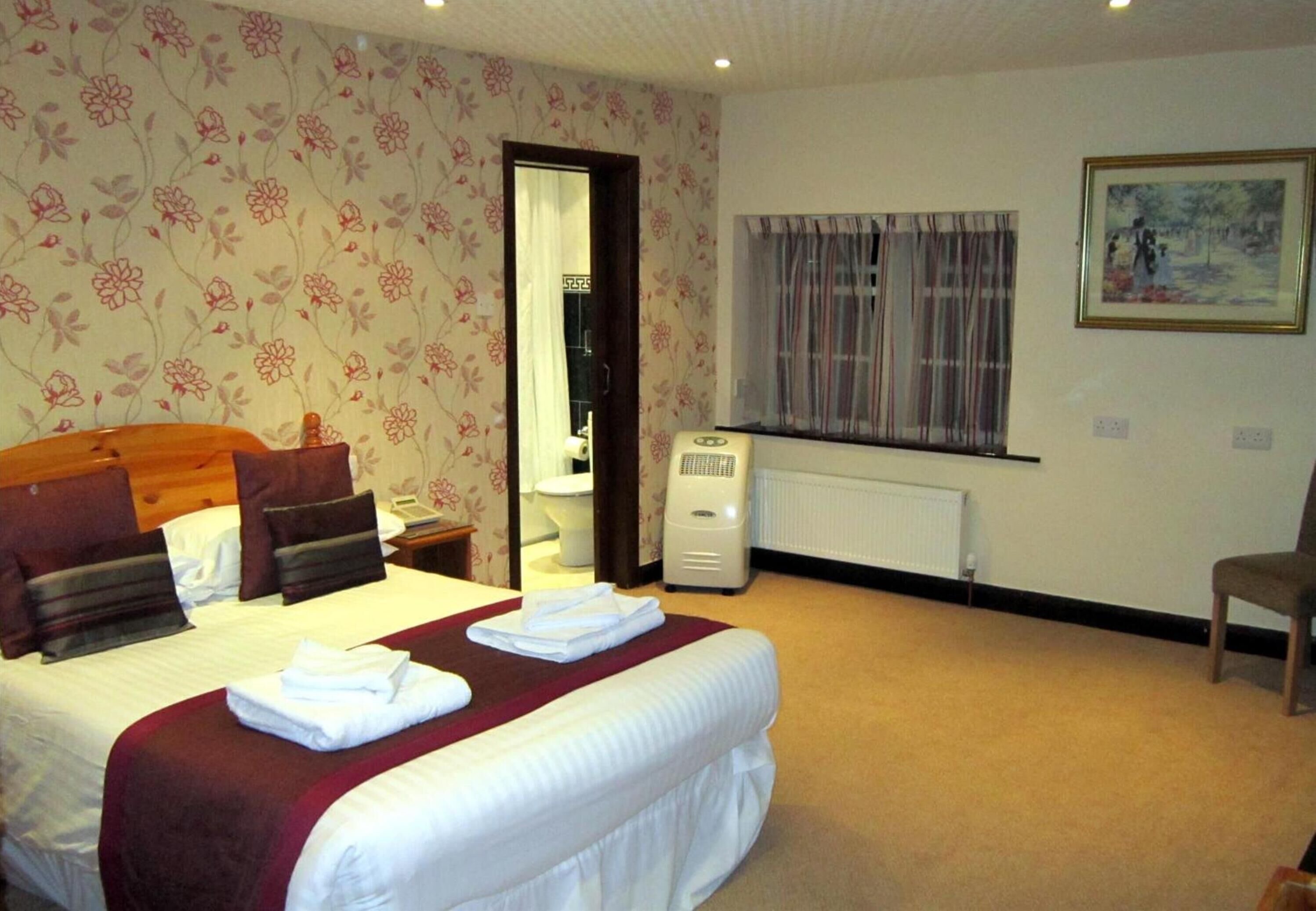 A hotel room with a large bed, a radiator, a window with curtains, and a painting on the wall.