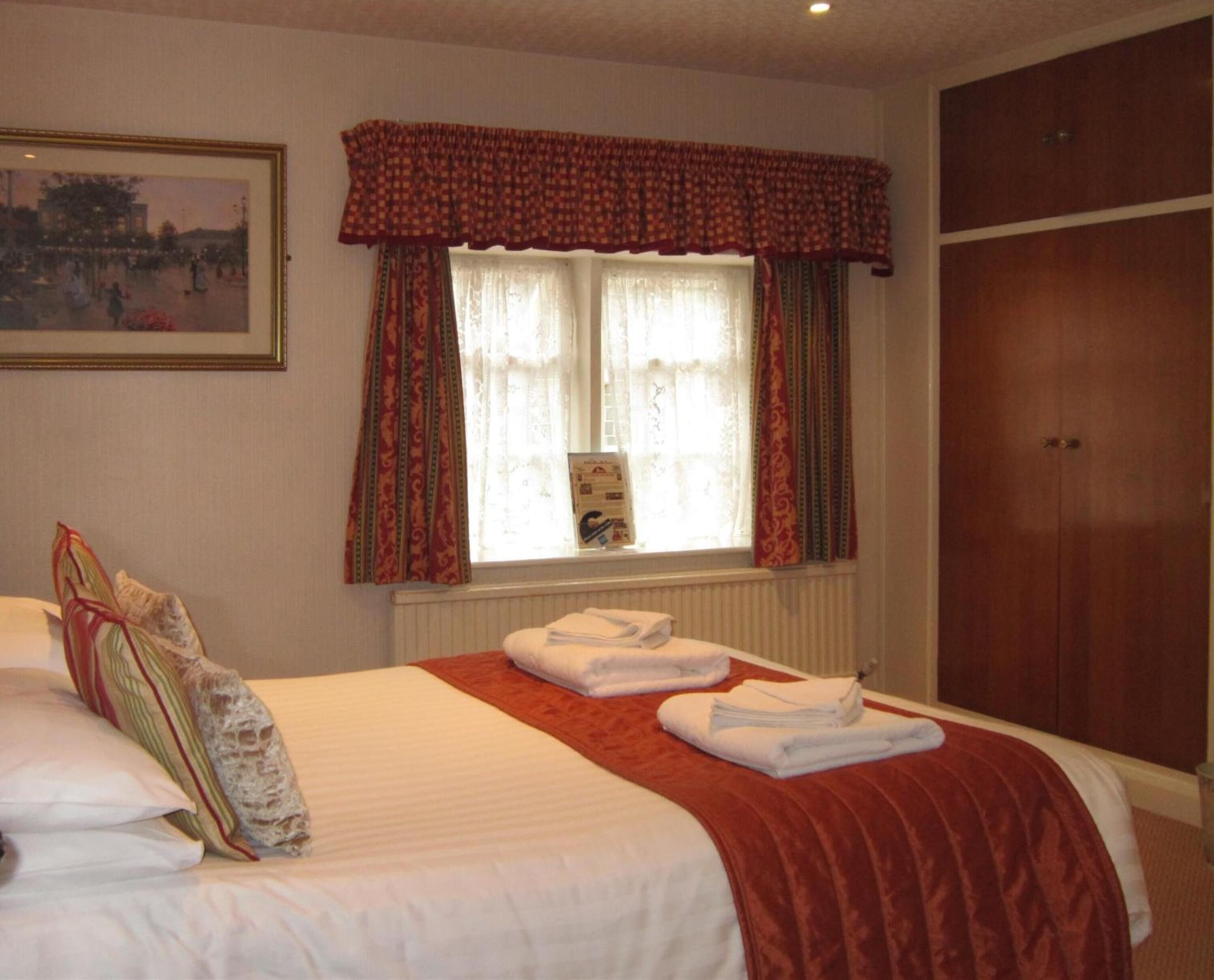 A hotel room with a bed, a window with curtains, a radiator, and a wardrobe.