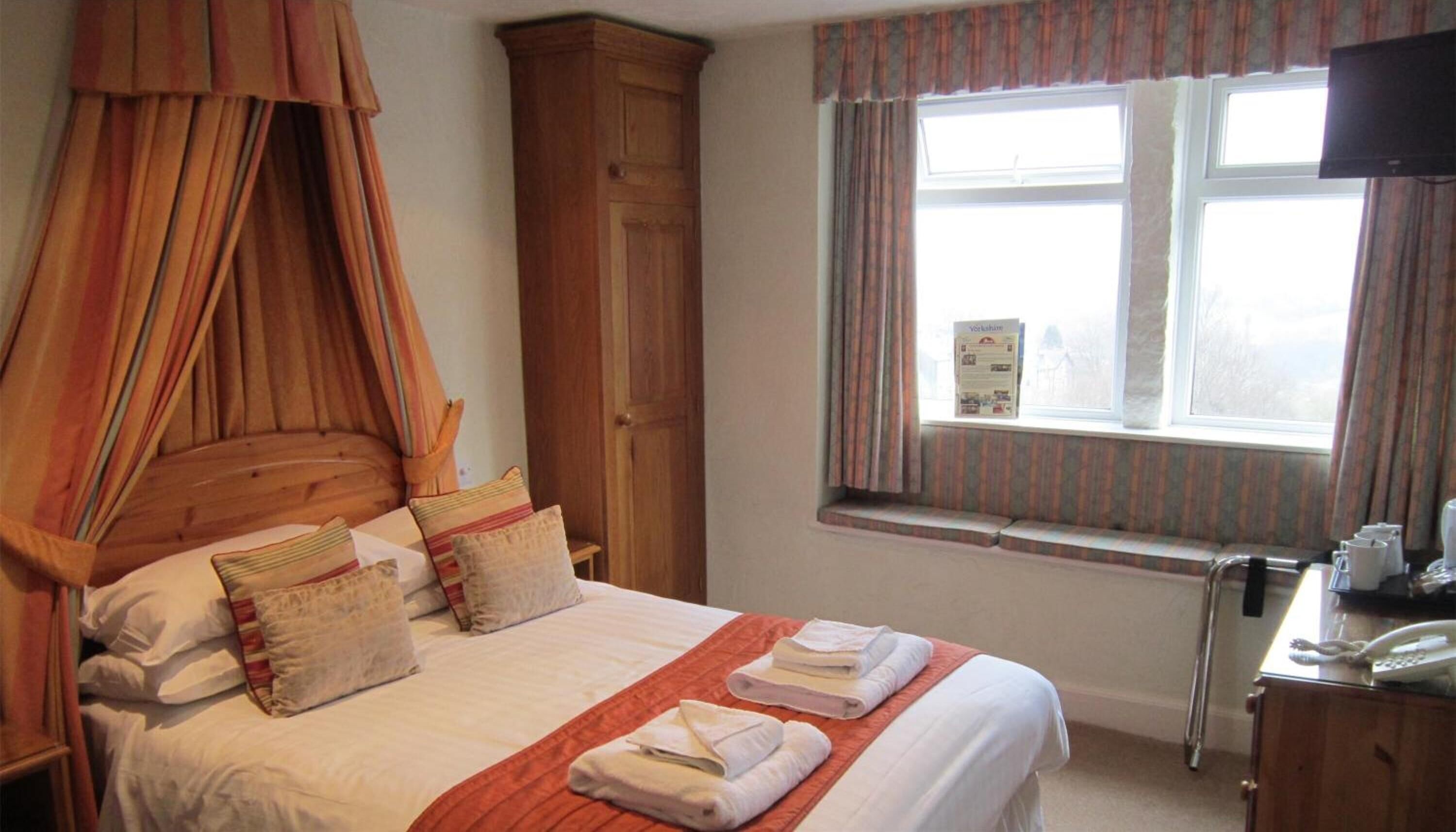 A bedroom with a canopy bed, a wooden wardrobe, a window with curtains, and a bedside table with a telephone.