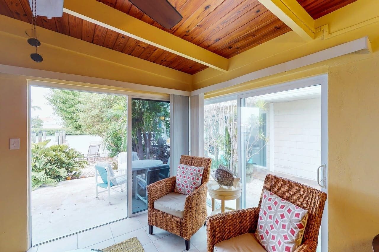 A room with wicker chairs, a small round table, and a sliding glass door leading to an outdoor patio with a table and chairs.