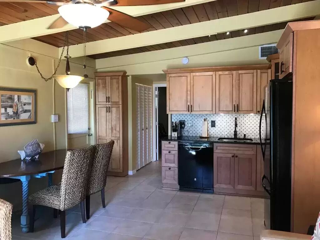 A kitchen with wooden cabinets, a black refrigerator, and a dining area with a table and chairs.