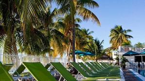 Eine Reihe von grünen Liegestühlen mit einem Pool und Palmen im Hintergrund.
