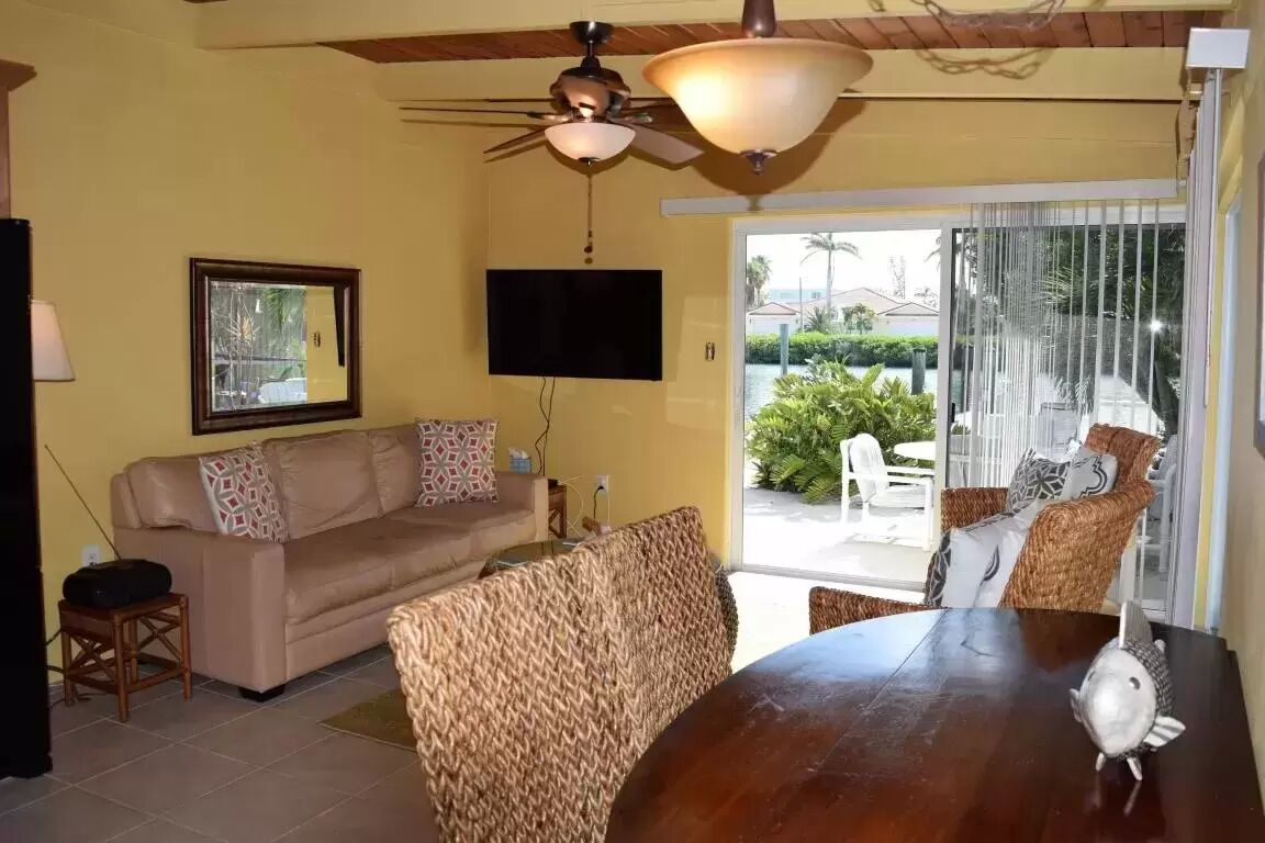 A living room with a sofa, a television, a ceiling fan, and a view of the outdoors.