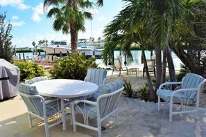 A patio with a round table and six chairs, surrounded by palm trees and a view of boats on the water.
