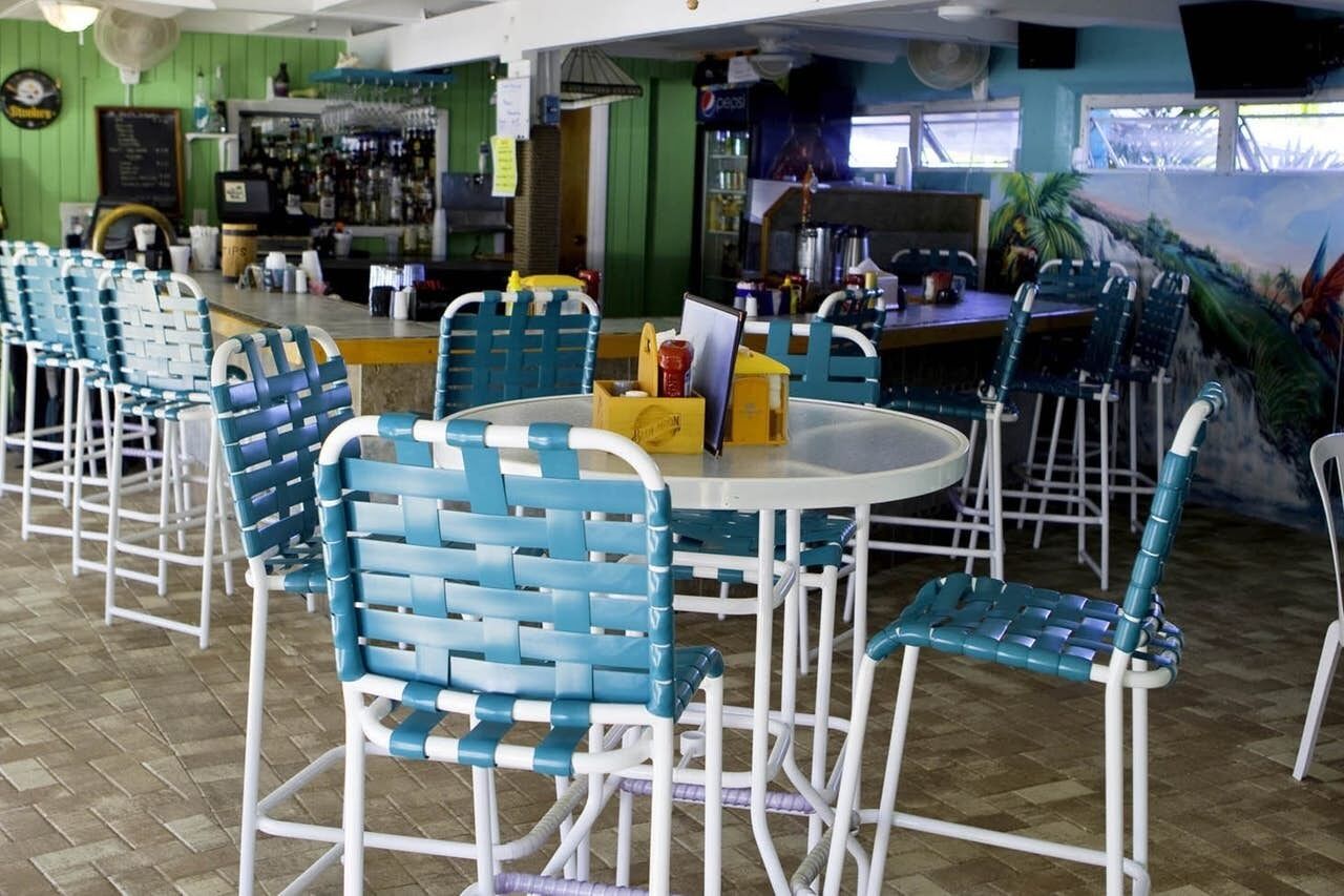 A restaurant with blue and white chairs, a round table, and a bar area in the background.